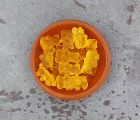 Bowl of colorful yellow gummi bear sugar candies on a gray background top view.