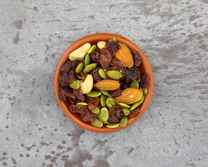 Small bowl filled with seeds, nuts and fruit on a gray background top view.