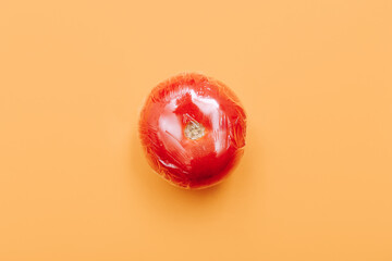 One tomato in wrap polyethylene plastic on orange background. Minimal enviromental concept. Flat...