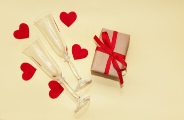 Glass elegant empty champagne glasses lie among decorative felt hearts and next to a gift box with a red ribbon. Copy space. Romance on Valentine's Day