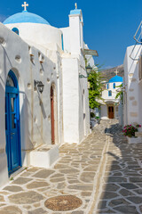 Traditional Cycladitic alley with a narrow street, a whitewashed churches  with a blue dome and  blooming flowers in parikia, Paros island, Greece.