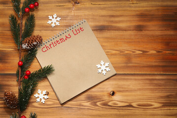 Notebook with the inscription: Christmas list and a beautiful branch of a fir tree with cones and berries on a wooden background. Christmas composition.
