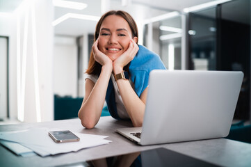 Happy smiling young woman sitting at desk with open laptop looking at camera. Successful smiling student girl staying at home using online learning tools and platforms.