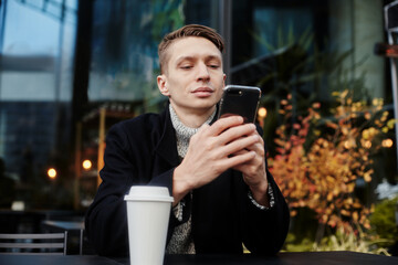 A man is sitting at a table in a cafe on the street Holding a Cup of coffee and chating