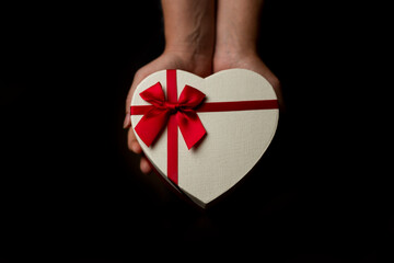 female hands holding a gift box in the form of a heart on a black background, isolate