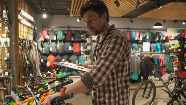 Sales assistant helps shopper choose bike at sporting goods store. Bicycle shop clerk advises customer. Male bicycle store owner talks about bicycles on camera. Man leads video blog about cycling