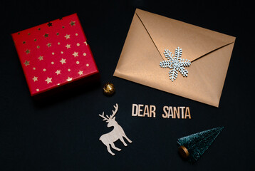 Dear Santa wooden letters on black background with Christmas decorations. Golden envelope and red gift box on dark background. Christmas concept. 