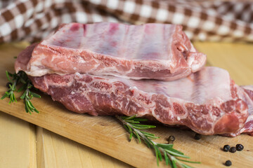 Uncooked pork ribs on a wooden board with rosemary and allspice peas on a kitchen towel background.