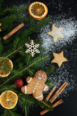 Naklejka premium Dark christmas background with snowflakes, spices, candy cane, fir tree and gingerbread cookies. Copy space for text.
