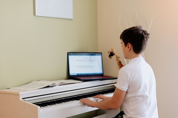 A young boy playing with sheet music on a white piano.