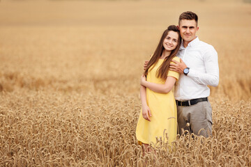 A young couple of lovers woman and man hugging in nature, in a yellow wheat field. The concept of love, good relationships, understanding and harmony