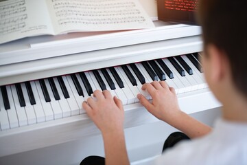 Fototapeta na wymiar Hands of a boy playing the piano with sheet music.