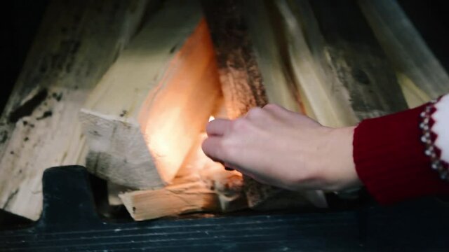 A woman lights a long-burning match and then ignites a fire in the fireplace