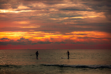 Sea sup surfing under amazing dark sunset sky. Two people on Stand Up Paddle Board. Orange sky. Paddleboarding Concept. Phuket. Thailand.