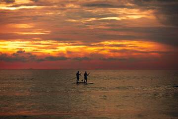 Sea sup surfing under amazing dark sunset sky. Two people on Stand Up Paddle Board. Orange sky. Paddleboarding Concept. Phuket. Thailand.