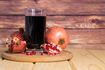 Fresh pomegranate juice in a glass glass, pomegranate fruits and pomegranate kernels on a wooden board on a wooden background. Copy space, space for text