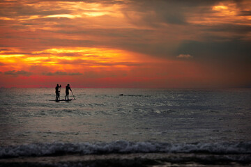 Sea sup surfing under amazing dark sunset sky. Two people on Stand Up Paddle Board. Orange sky. Paddleboarding Concept. trips to warm destinations.  Phuket. Thailand.