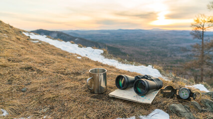 Binoculars map compass and mug on the background of nature mountains in the sunset. The concept of a halt, tourism travel, trip. Navigation, route