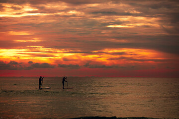 Sea sup surfing under amazing dark sunset sky. Two people on Stand Up Paddle Board. Orange sky. Paddleboarding Concept. Phuket. Thailand.