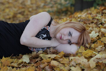 Kobieta blondynka leży w jesiennych liściach - obrazy, fototapety, plakaty