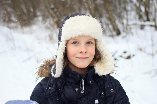 Winter portrait of young local Russian boy wearing traditional ushanka hat made of artificial fur