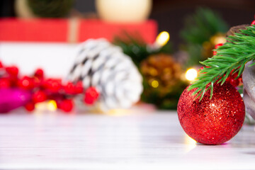 Red shiny Christmas ornament standing on white background in front of cones, gift box and New Year decorations. It is christmas concept!
