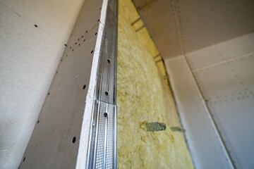 Wall of a room under renovation with mineral rock wool insulation and metal frame prepared for drywall plates.