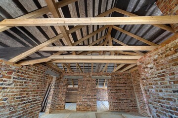 Attic of a building under construction with wooden beams of a roof structure and brick walls.