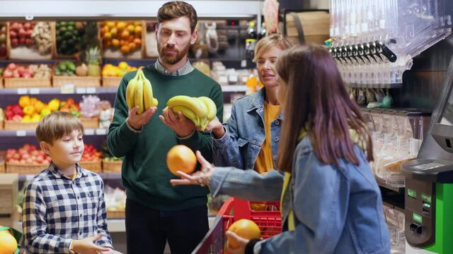 Young adult parents couple with two kids shopping in supermarket chosing organic product fruits communcioating on weekend food shopping.