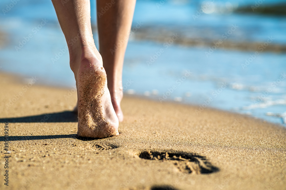 Wall mural close up of woman feet walking barefoot on sand leaving footprints on golden beach. vacation, travel