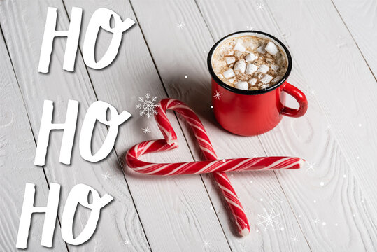 Red cup of cocoa near christmas candy canes near ho ho ho lettering on wooden - Powered by Adobe