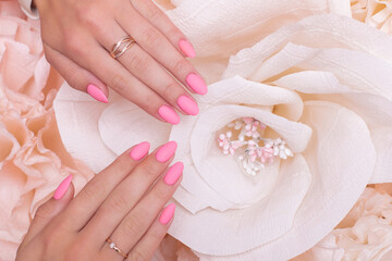 Female hands with wedding manicure nails, pink gel polish, on paper flowers background
