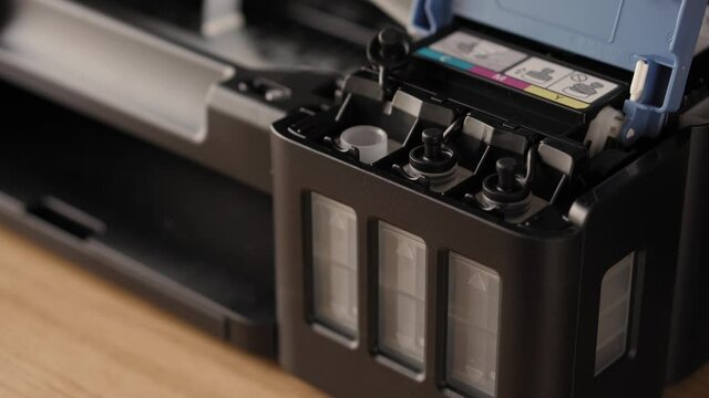 Video instruction, technology, media, office, stationery concept - close-up of male hands preparing new inkjet printer for launch. step 10: insert nozzle of bottle into inlet stand upside down pur ink