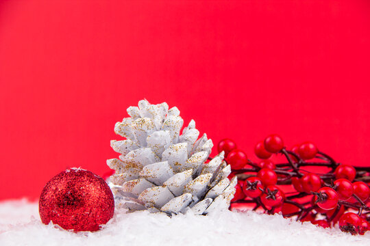 Close up red kokina flower, white pine cone and bright red new year ornament on red background and snowy backdrop for Christmas