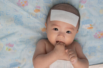 Unhappy Asian Chinese little baby child sick suffering heat from fever with cool fever jel pad on...