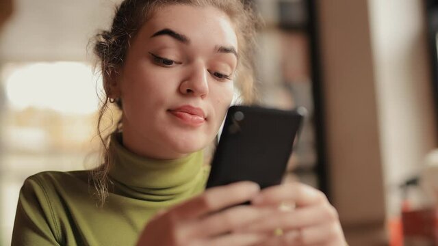Young woman using mobile phone in a cafe drinking tea