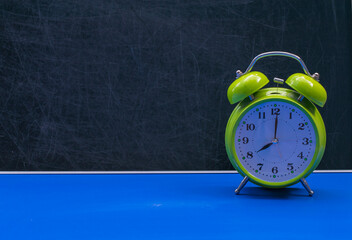 Alarm clock with the time 8.00 on a blue table against the background of a school board. The...