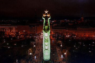 Riga,Latvia - 18 November 2020: Monument of freedom at night in Riga, Latvia during Staro Riga event. Milda - Statue of liberty holding three stars over the city illuminated in different colors.