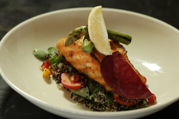 Delicious quinoa salad with roasted salmon and vegetables. Appetizing healthy dish in restaurant. Culinary art concept.