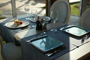 Served dinner table at restaurant. Table served with plates, wine glasses, knives and forks. Tasty sweets are on table.