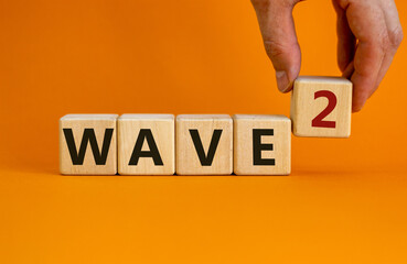 Symbol for a second wave of the corona virus. Hand holds a cube. Words 'wave 2'. Covid-19 pandemic...