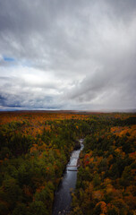 Beautiful aerial above the Bad River and a pedestrian foot bridge at Copper Falls with colorful fall foliage lining the river banks and cloudy sky above the horizon in autumn in Mellen, Wisconsin.