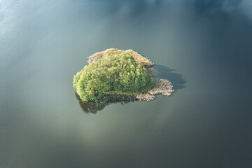 Aerial view of small island on the lake and clouds and sky reflecting in water, green toned image