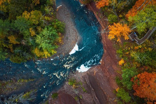 Beautiful travel look down photograph of a curved river bend lined with a red dirt cliff and colorful autumn tree leaves or foliage on the Potato River in Wisconsin.