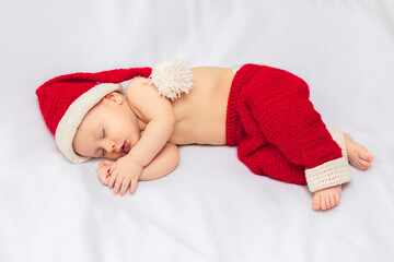 Innocent baby wearing handmade crocheted red christmas elf hat and pants, sleeping on white fleece...