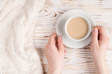 Good morning winter concept. Top above overhead close up view photo of female hands holding cup of tasty fresh latte on wooden desk with knitted blanket