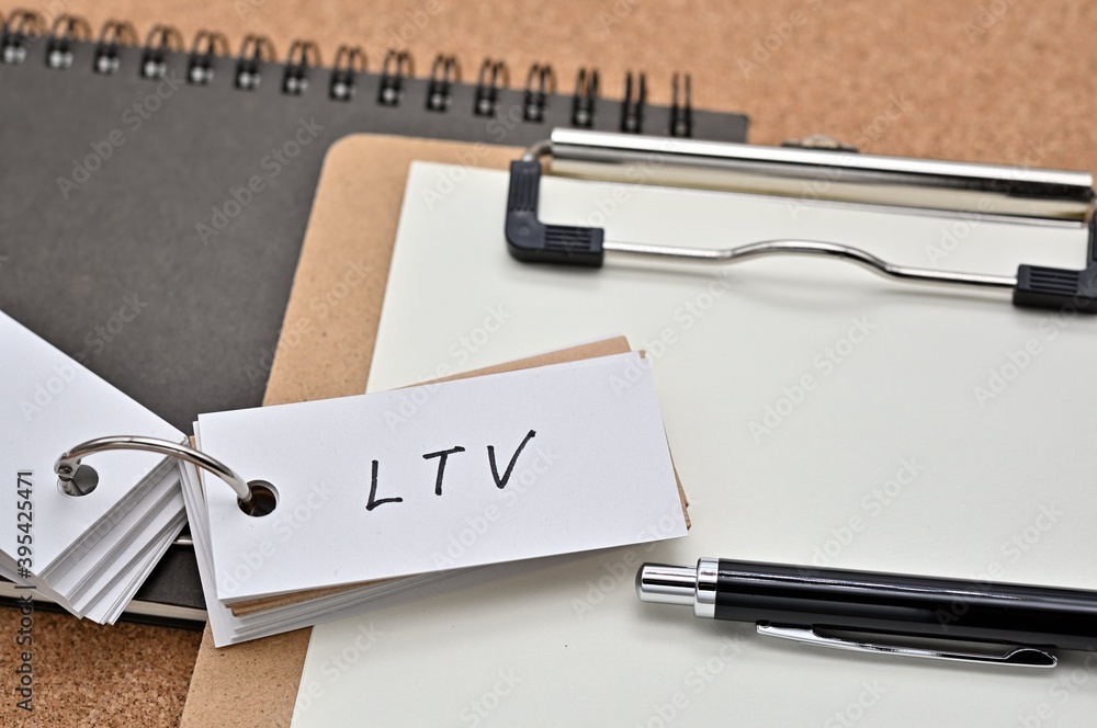 Poster on top of the notebook and clipboard is a wordbook and pen with the word ltv written on it. it means