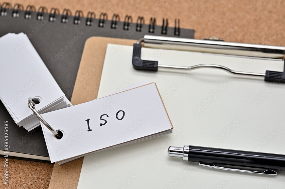 Poster on top of the notebook and clipboard is a wordbook and pen with the word iso written on it. it means
