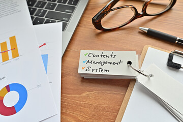 There is a piece of paper with a graph printed on it, a clipboard, and an open vocabulary book on the desk. There is the word Contents Management System on it.