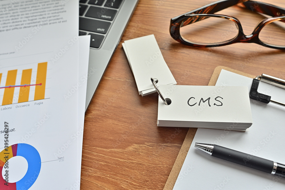 Poster on top of the notebook and clipboard is a wordbook and pen with the word cms written on it. it means